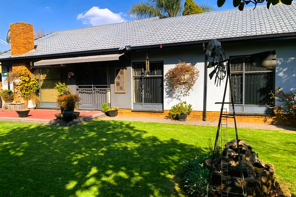 Rear view of the house featuring a tiled roof, brick chimney, paved patio area, and well-maintained garden with security features on windows and doors.