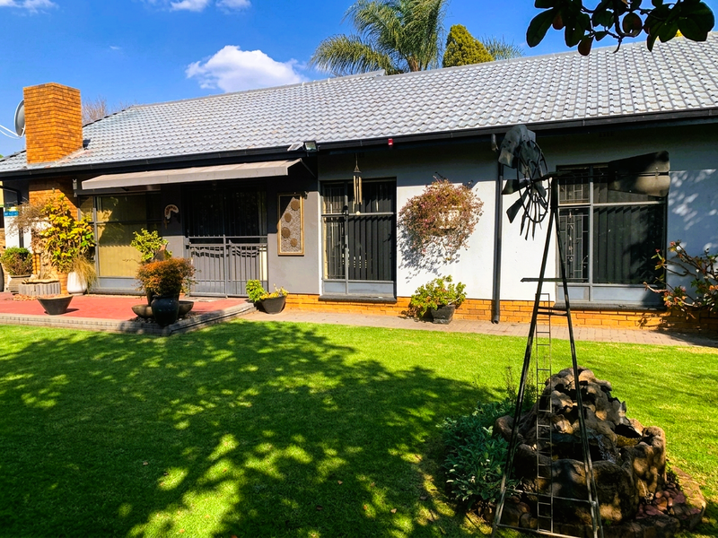 Rear view of the house featuring a tiled roof, brick chimney, paved patio area, and well-maintained garden with security features on windows and doors.