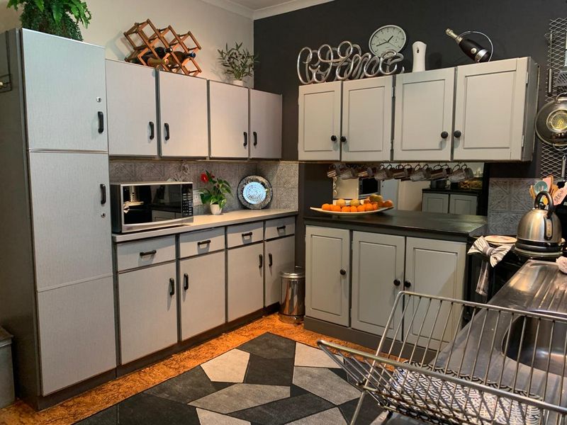 A functional kitchen featuring grey built-in cabinetry, tiled backsplash, and laminate countertops, providing ample storage and workspace.