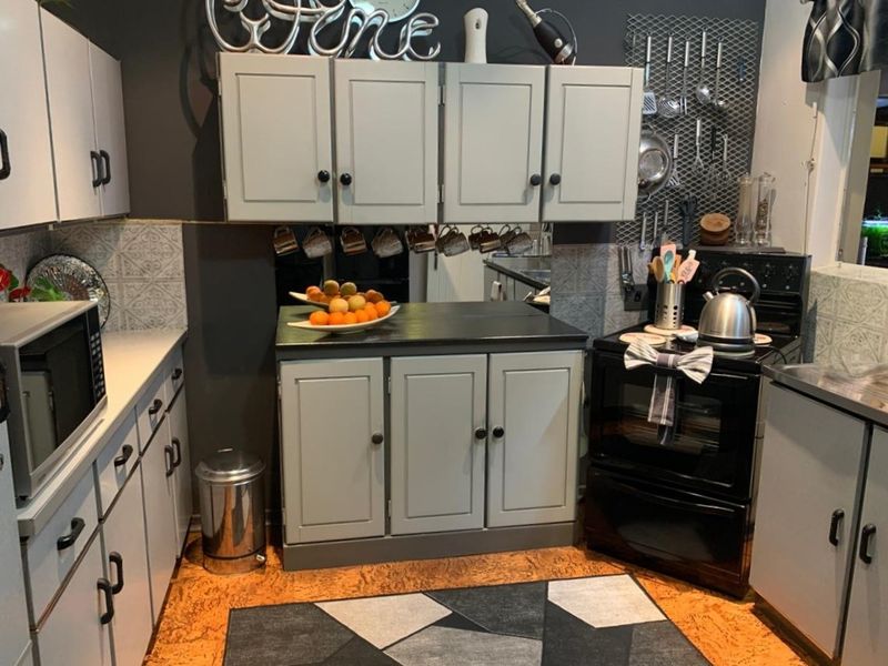 A compact kitchen featuring grey cabinetry, black countertops, a built-in oven, and a decorative tiled backsplash.