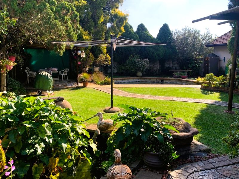 A lush, established garden featuring a swimming pool, a small pond, and paved walkways, offering a private outdoor space for relaxation.