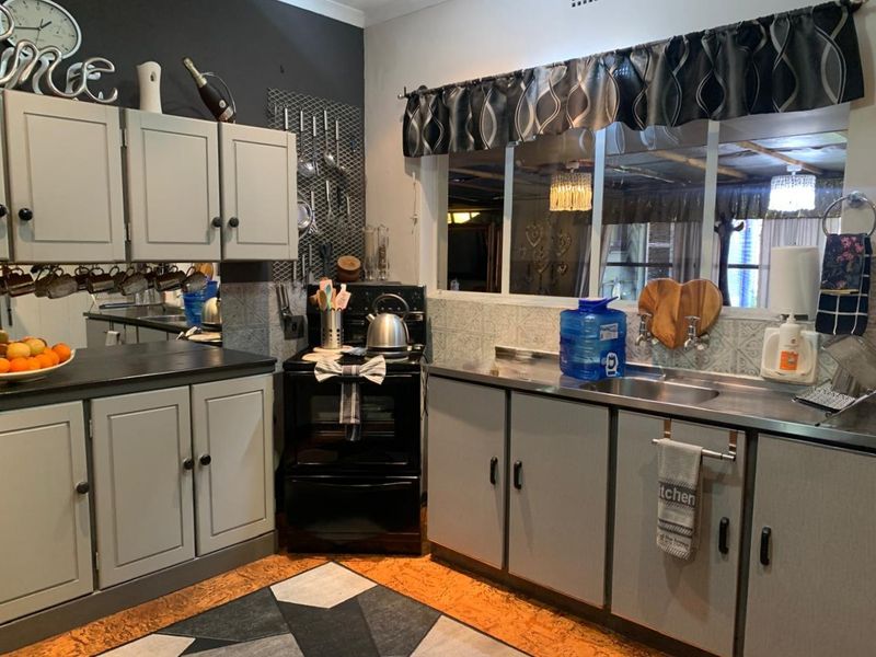 A functional kitchen featuring grey cabinetry, stainless steel sink, and a freestanding stove with a tiled splashback.