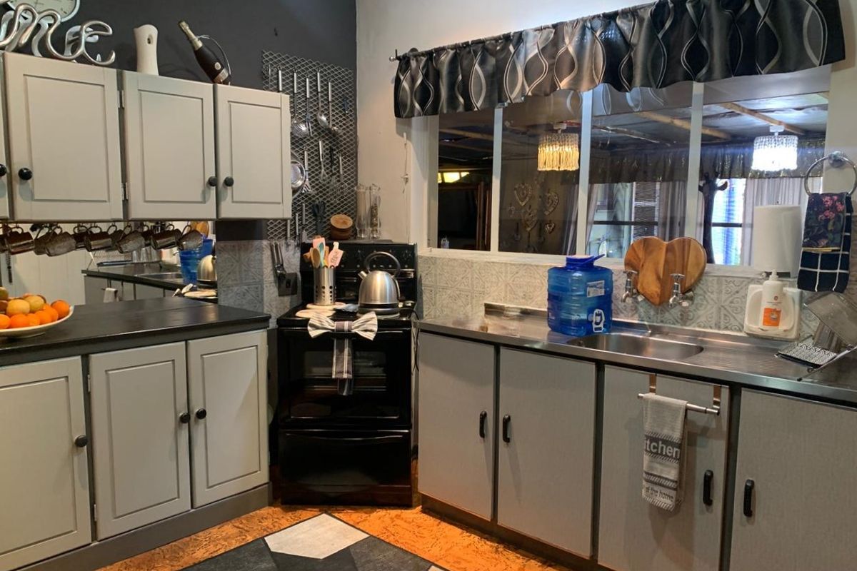 A functional kitchen featuring grey cabinetry, stainless steel sink, and a freestanding stove with a tiled splashback.