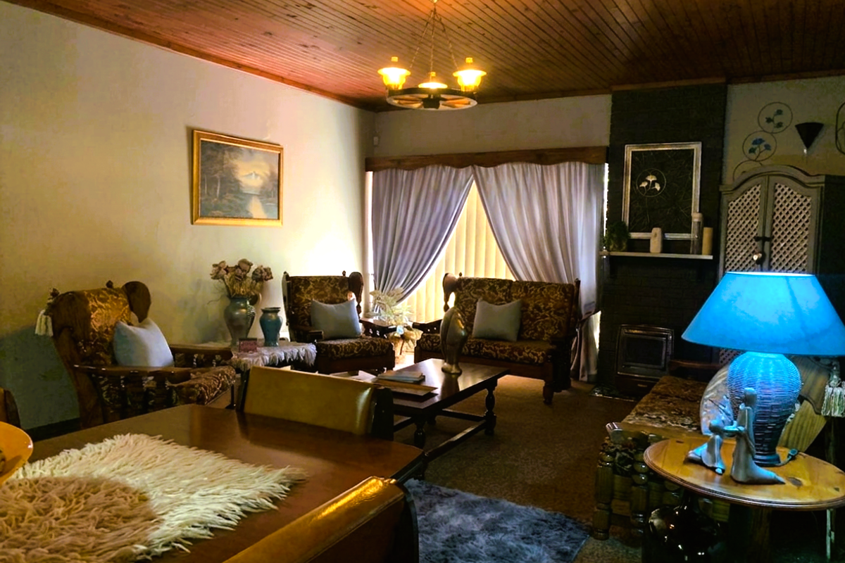 A traditional living room featuring a timber-clad ceiling, a brick fireplace with an integrated insert, and a large window with a timber pelmet.