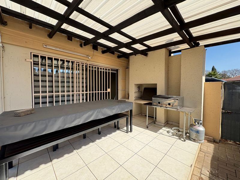 Covered patio area featuring a built-in braai, tiled flooring, and a timber pergola, providing a functional outdoor entertainment space.