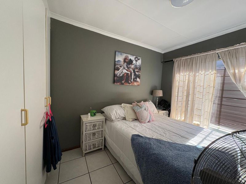 A bedroom featuring tiled flooring, built-in cupboards, and a neutral color palette, offering a functional space with natural light from the window.