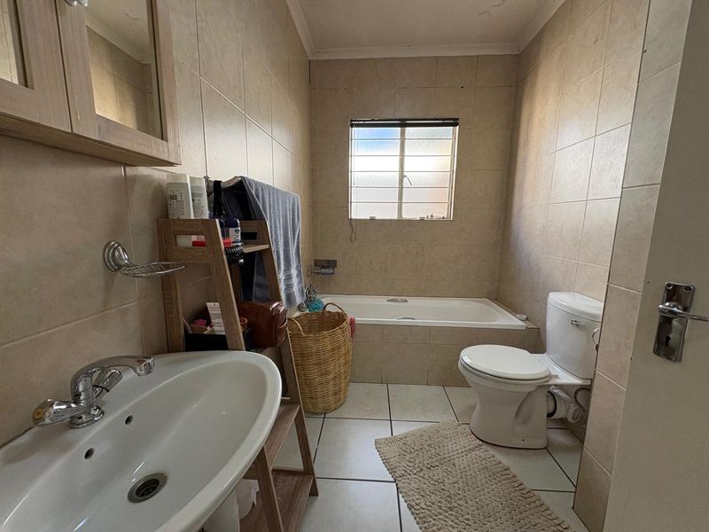 A functional bathroom featuring a built-in bathtub, pedestal basin, and toilet, finished with neutral ceramic wall and floor tiles.