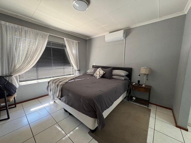 A well-lit bedroom featuring tiled flooring, an installed air conditioning unit, and venetian blinds for privacy.