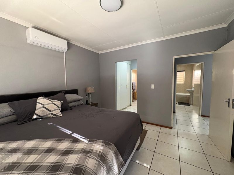 Spacious bedroom featuring tiled flooring, a wall-mounted air conditioning unit, and direct access to an en-suite bathroom and built-in storage area.