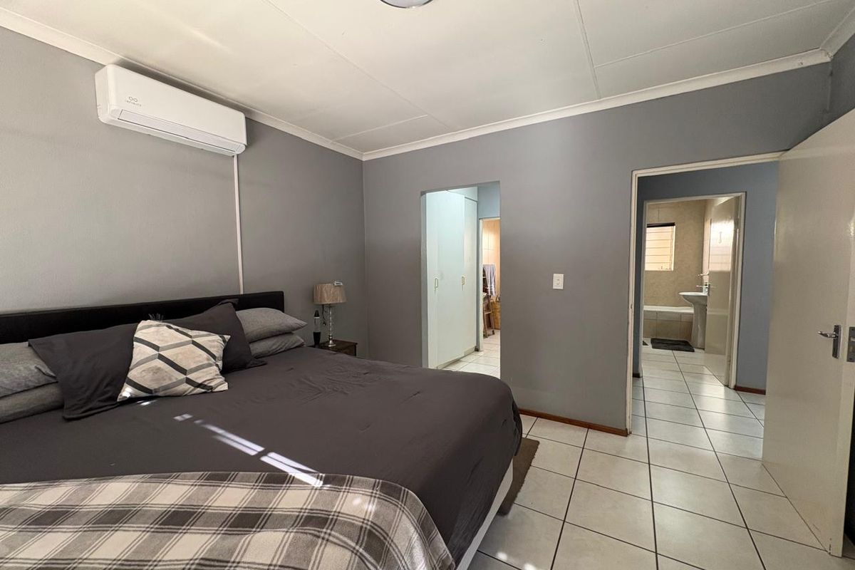 Spacious bedroom featuring tiled flooring, a wall-mounted air conditioning unit, and direct access to an en-suite bathroom and built-in storage area.
