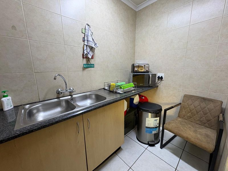 A functional scullery area featuring a double stainless steel sink, laminate cabinetry, granite countertops, and full-height ceramic wall tiling.