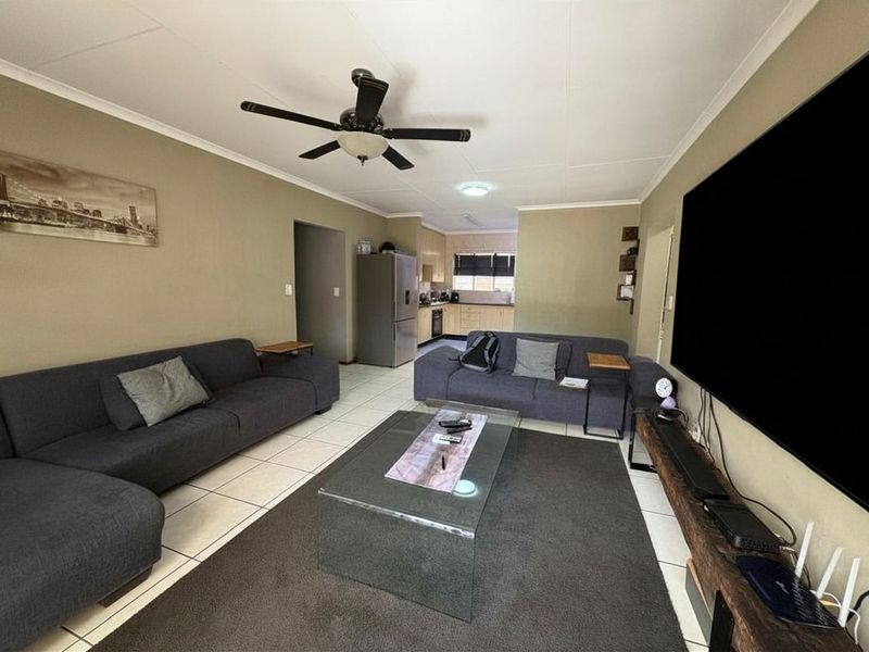 Open-plan living area featuring tiled flooring, a ceiling fan, and a functional kitchen space with built-in cabinetry and appliances.