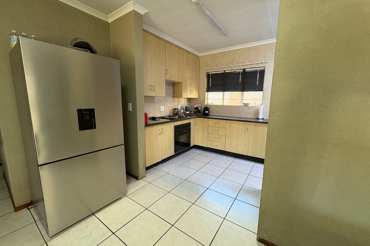 Functional kitchen featuring light wood-finish cabinetry, dark countertops, built-in oven, hob, and tiled flooring with a neutral backsplash.