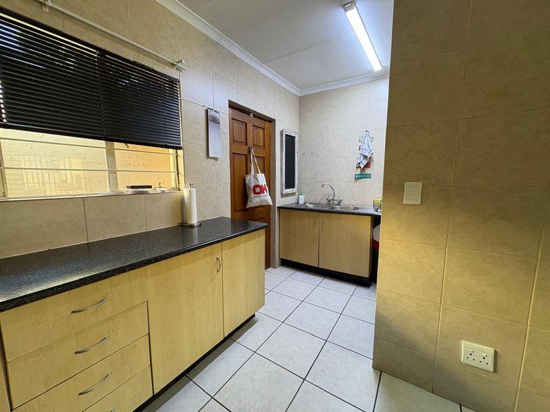 A functional scullery area featuring laminate cabinetry, granite countertops, a stainless steel sink, and neutral ceramic tiling throughout.
