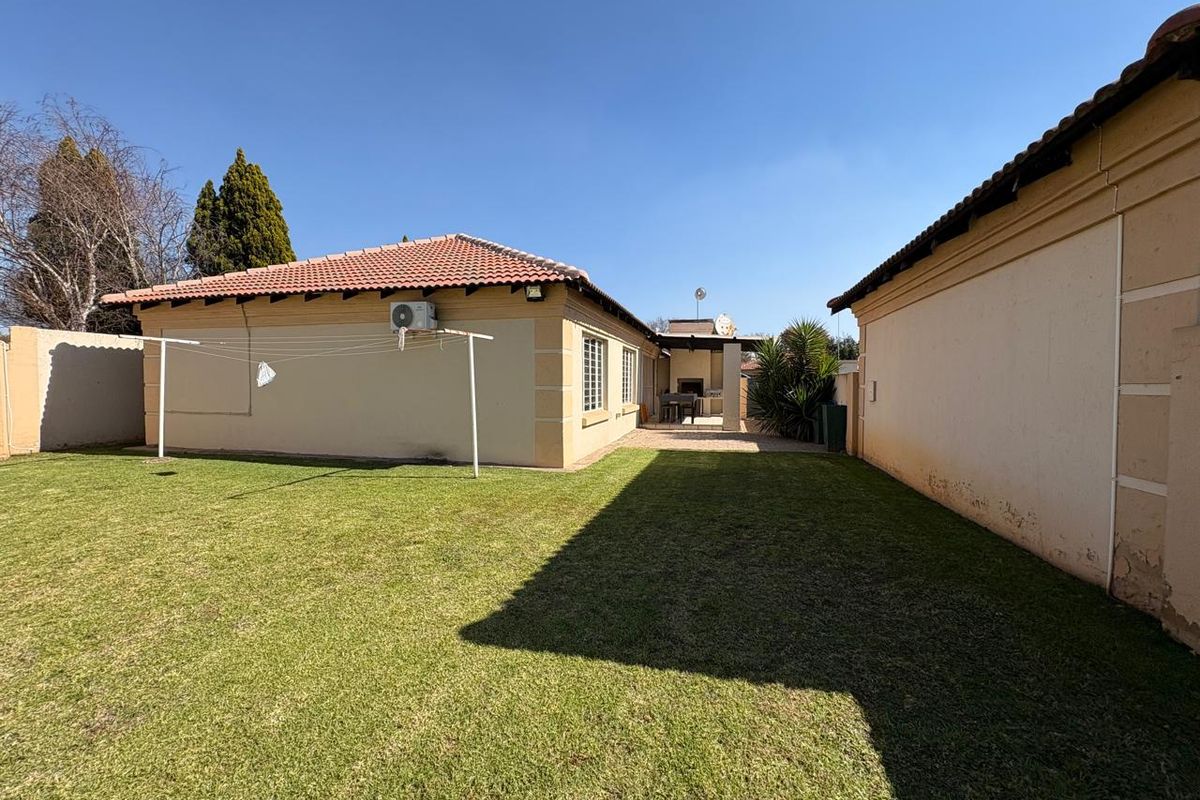 Rear view of the townhouse featuring a private garden, lawn, covered patio with a built-in braai, and exterior wall-mounted air conditioning unit.