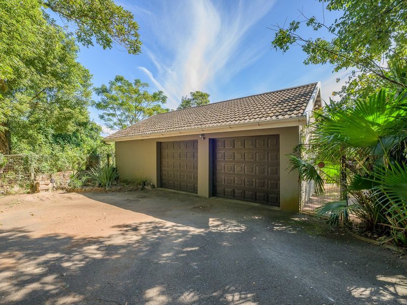 A detached double garage featuring brown panelled doors, a tiled roof, and an asphalt driveway, set within a mature garden environment.