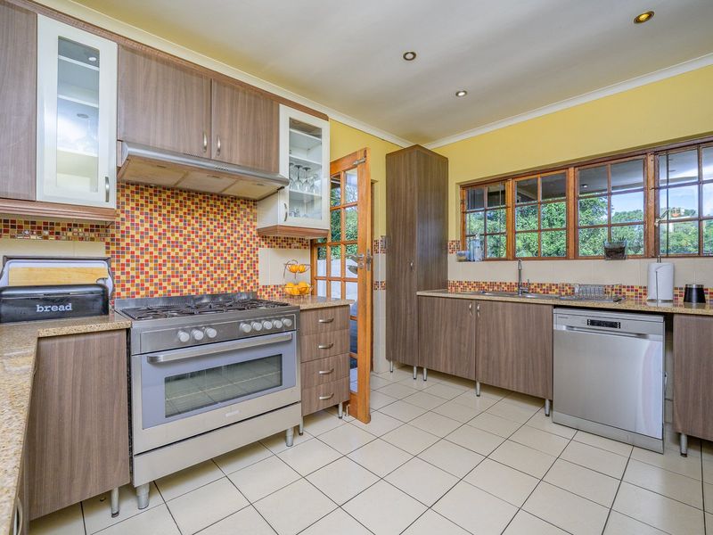 A functional kitchen featuring wood-finish cabinetry, granite countertops, a gas stove with extractor, and a mosaic tile backsplash with tiled flooring.