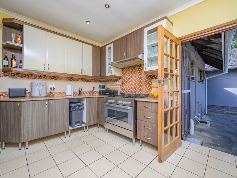 A functional kitchen featuring wood-tone cabinetry, granite countertops, a gas stove with extractor fan, and direct access to an exterior side area.
