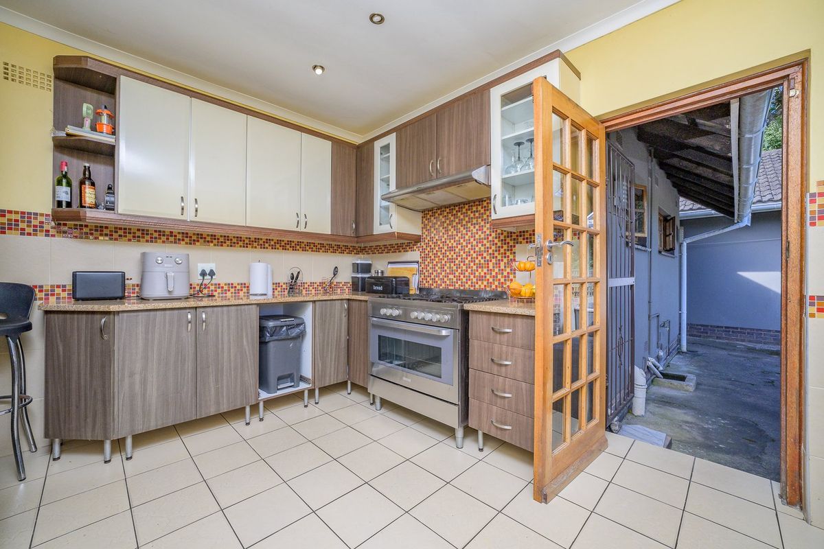 A functional kitchen featuring wood-tone cabinetry, granite countertops, a gas stove with extractor fan, and direct access to an exterior side area.