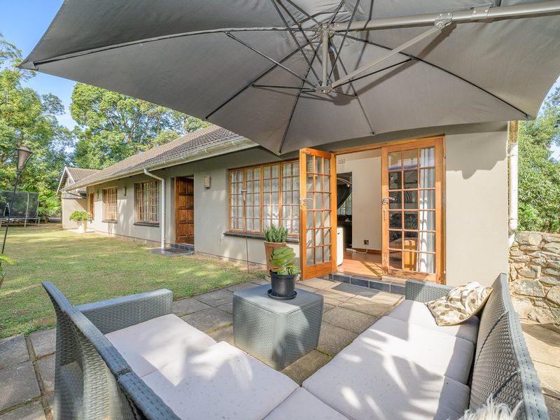 A paved outdoor patio area featuring timber-framed glass doors providing direct access to the home, set against a landscaped garden and stone retaining wall.
