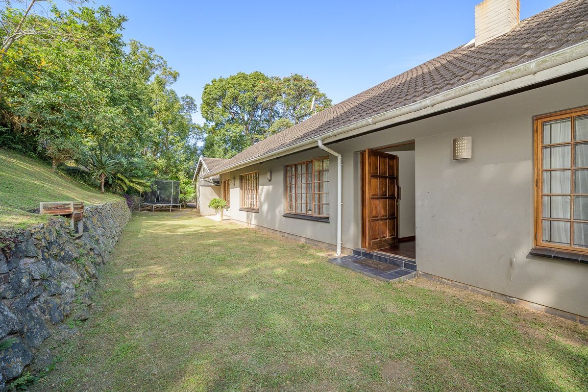 Rear view of the house featuring a lawn, stone retaining wall, and access to the interior through a timber door.