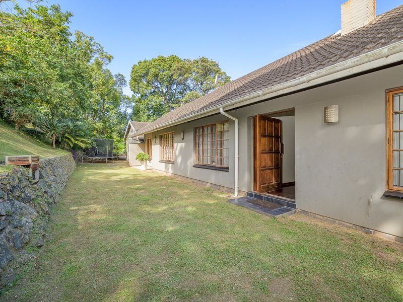 Rear view of the house featuring a lawn, stone retaining wall, and access to the interior through a timber door.