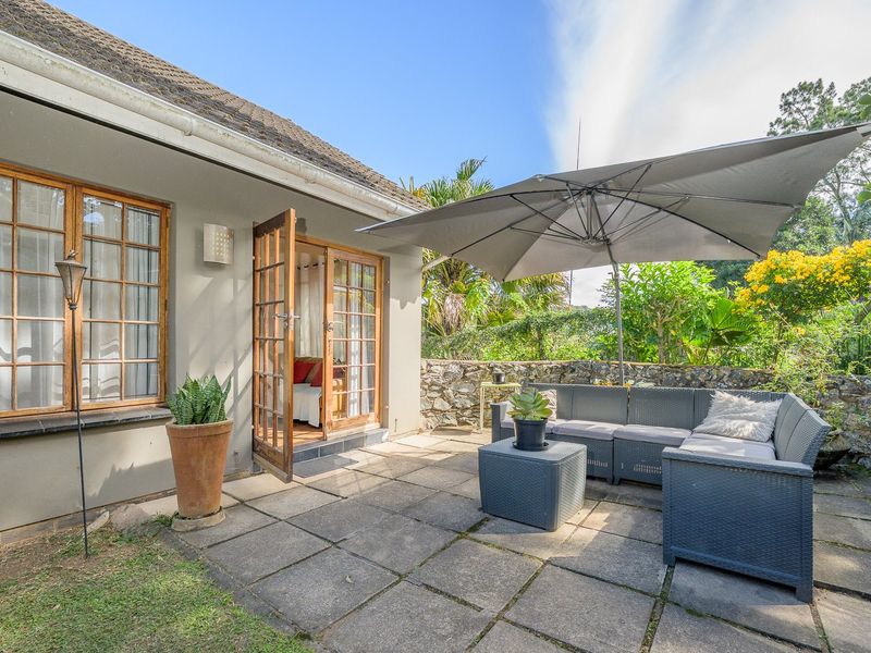A paved outdoor patio area featuring a stone retaining wall and direct access to the interior through timber-framed glass doors.