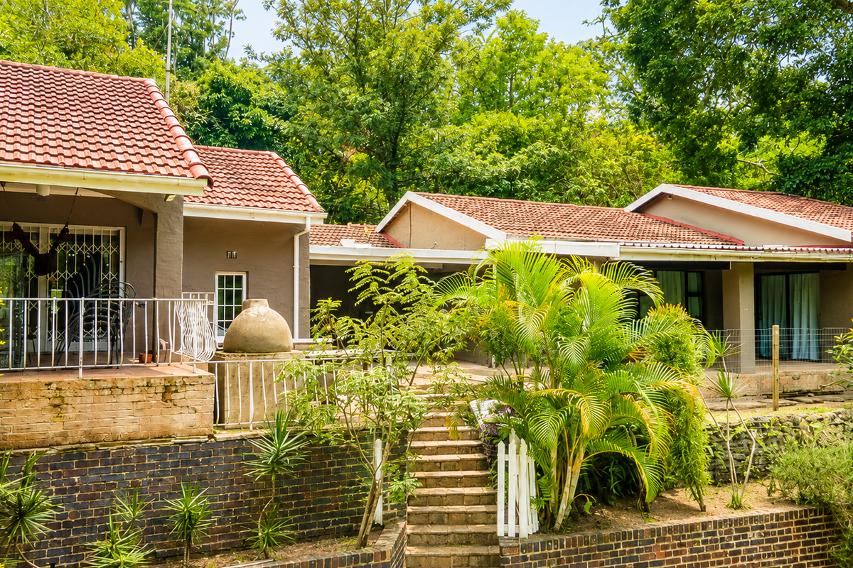 Rear view of the property featuring a covered patio, stone staircase, built-in pizza oven, and tiered brick retaining walls set against a lush garden.