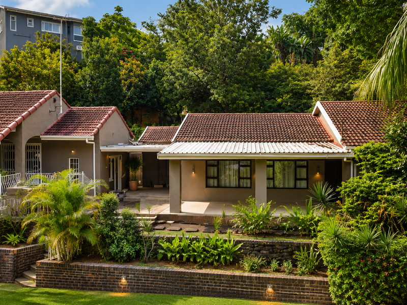 A well-maintained rear exterior view featuring a covered patio, terracotta roof tiles, and tiered brick retaining walls set within a lush, landscaped garden.