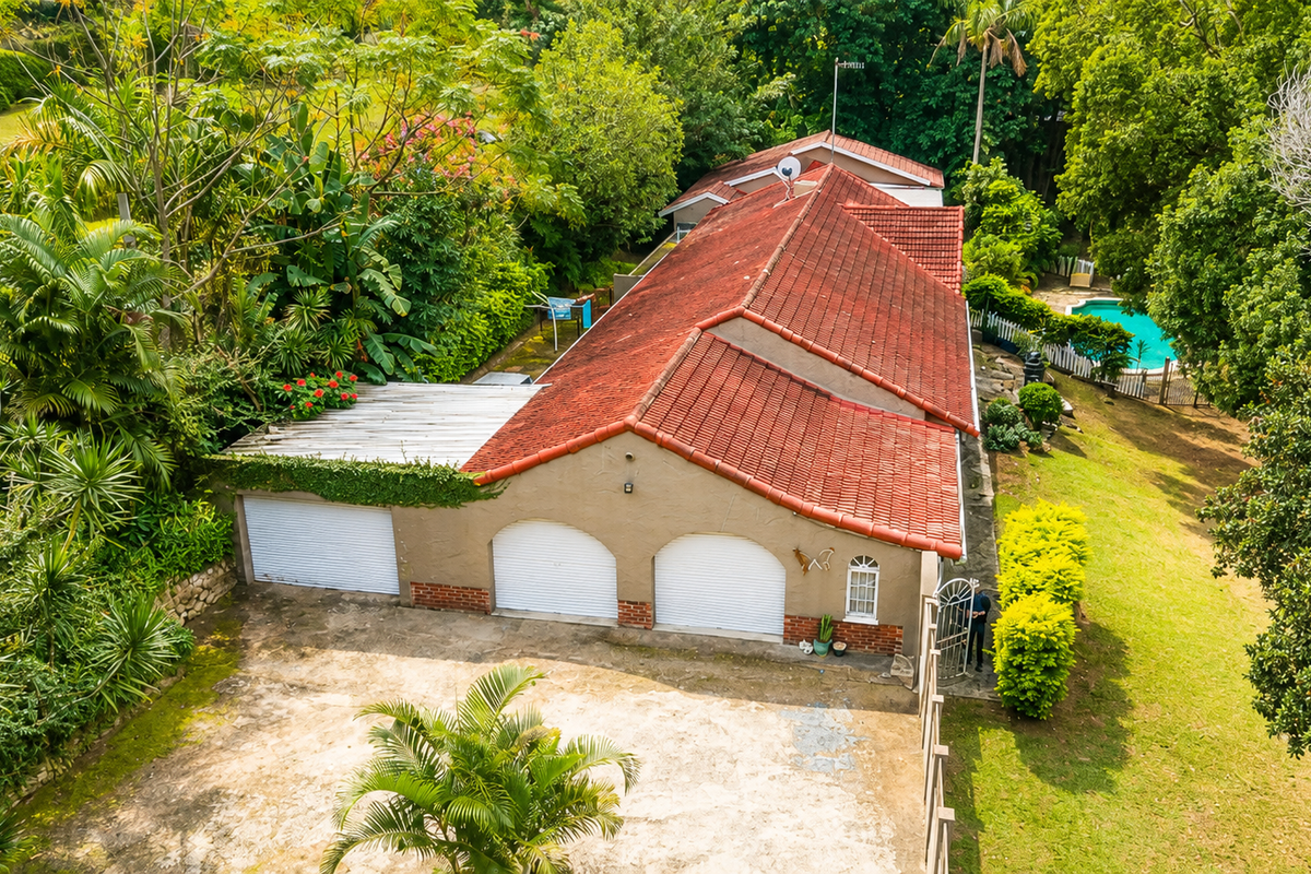Aerial view of a residential property featuring a triple garage, terracotta tiled roof, swimming pool, and established garden surroundings.