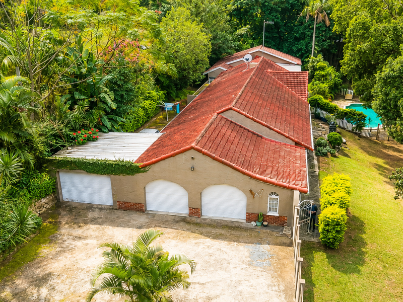 Aerial view of a residential property featuring a triple garage, terracotta tiled roof, swimming pool, and established garden surroundings.
