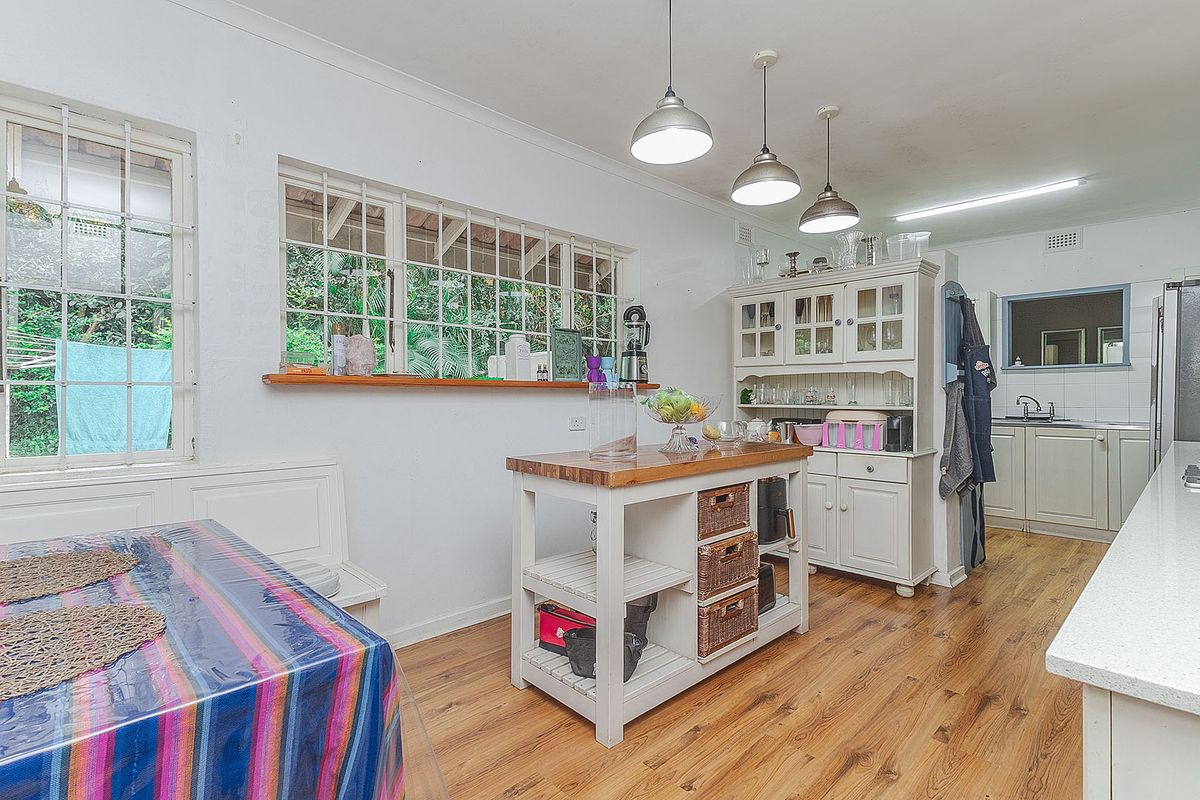 A functional kitchen featuring timber flooring, ample cabinetry, pendant lighting, and large windows with security bars, offering a bright and practical workspace.