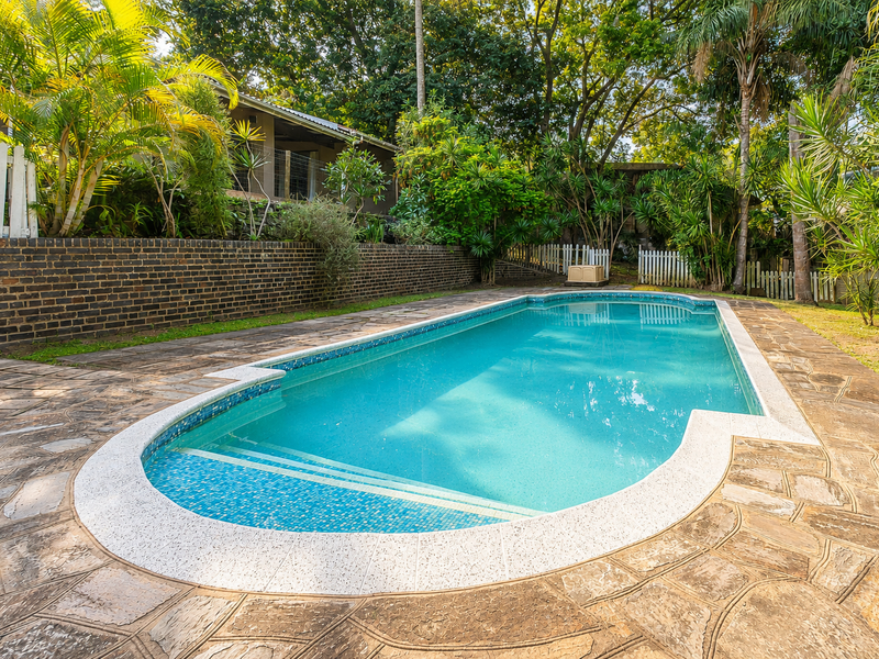 A well-maintained swimming pool area featuring stone paving, a brick retaining wall, and lush garden surroundings.