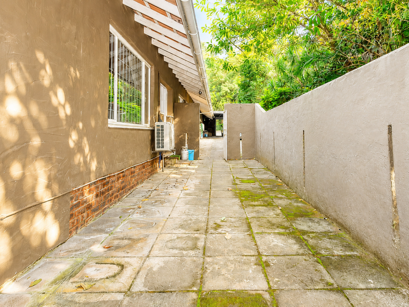 A narrow paved side passage along the rear of the house, featuring a boundary wall and an external air conditioning unit.