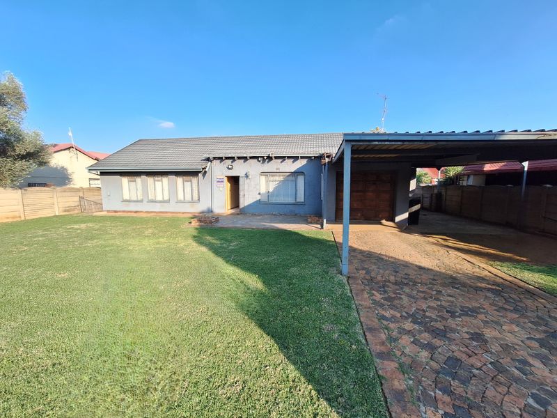 Front view of a single-story house featuring a tiled roof, attached carport, paved driveway, and a well-maintained front lawn.