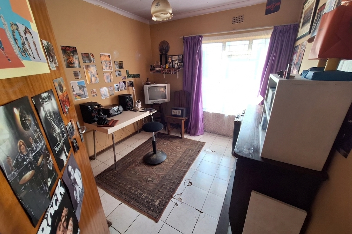A bedroom featuring tiled flooring and a window with security bars, currently requiring maintenance due to damaged floor tiles.
