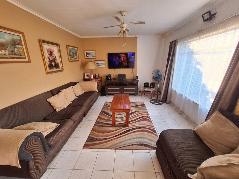 A living room featuring tiled flooring, a ceiling fan, and a large window. The space requires cosmetic updates to the wall finishes and flooring.