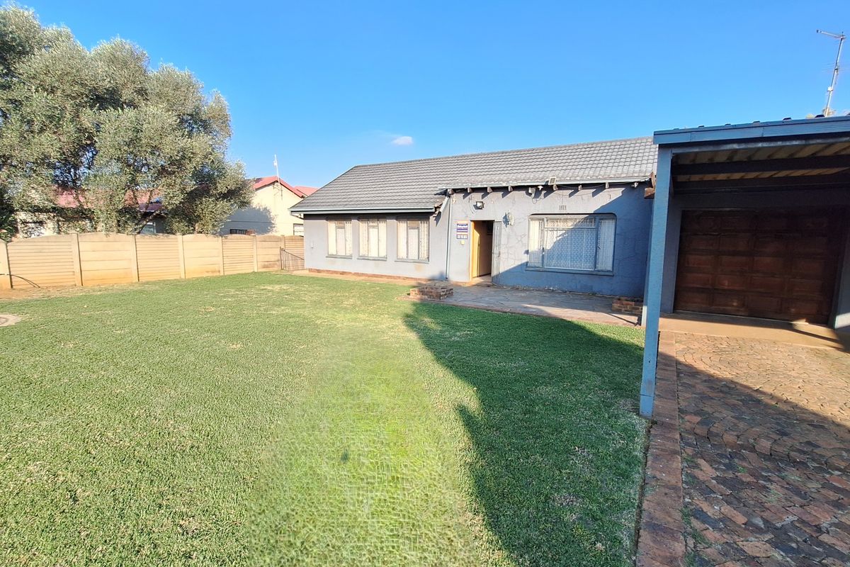 Rear view of the property featuring a spacious lawn, paved driveway, carport, and a tiled roof structure with security bars on windows.