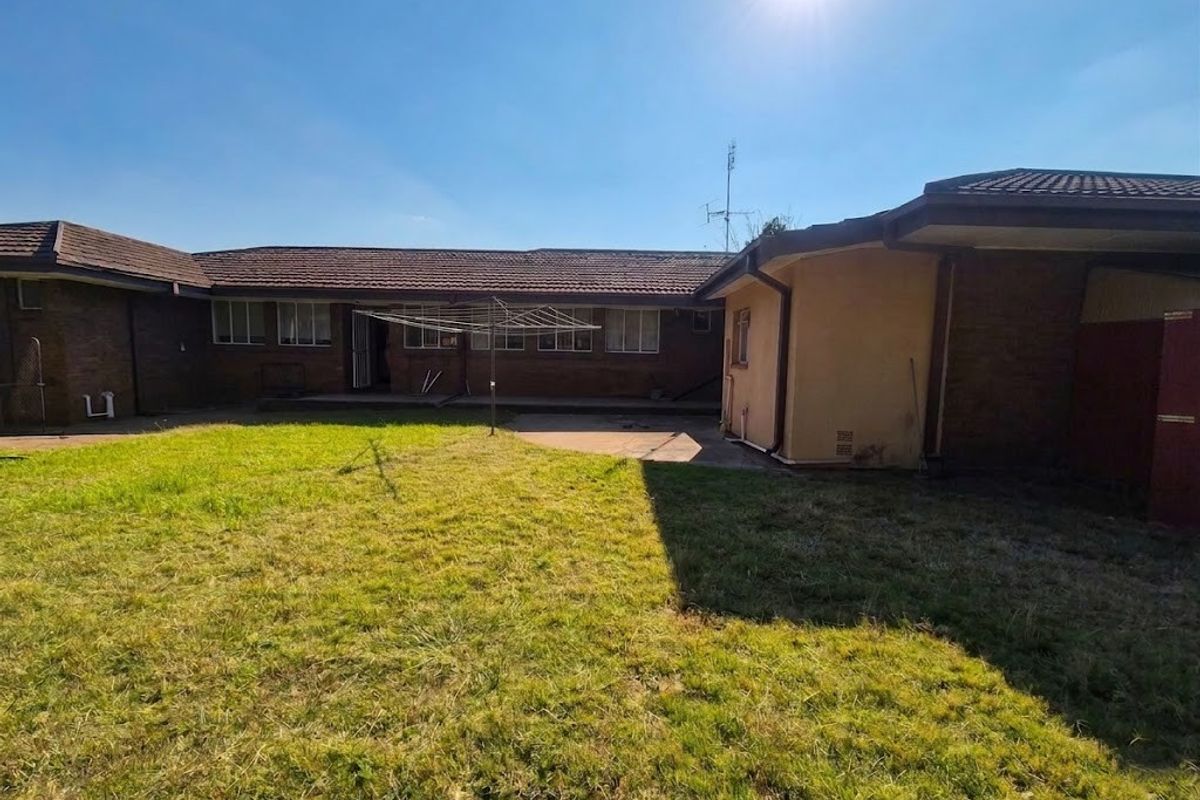 A view of the rear exterior of the house featuring a brick facade, tiled roof, concrete patio area, and a spacious backyard lawn.