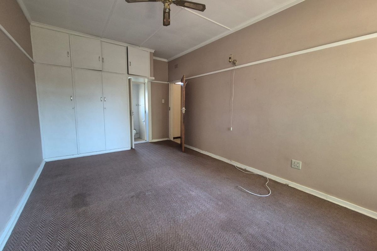 Spacious bedroom featuring built-in cupboards, a ceiling fan, and carpeted flooring. The room is vacant and ready for renovation or restyling.