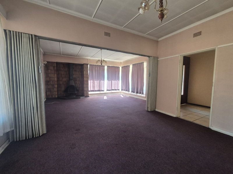 Spacious, empty living area featuring a classic freestanding fireplace, folding room dividers, and neutral carpeting, offering a blank canvas for renovation.