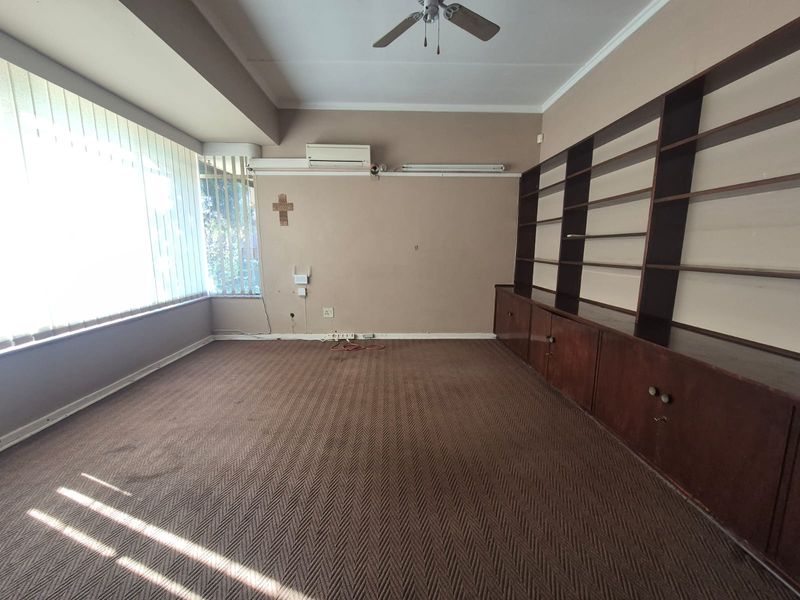 Spacious living room featuring built-in wooden shelving, a ceiling fan, and a split-system air conditioner, offering a blank canvas for renovation.
