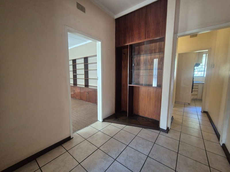 A spacious hallway featuring built-in wooden cabinetry and tiled flooring, providing access to adjacent living and kitchen areas.