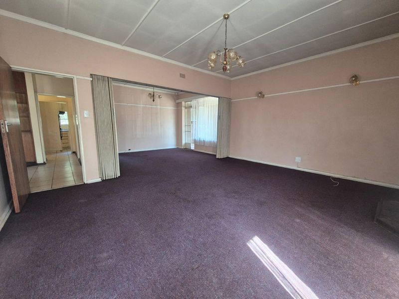 Spacious living area featuring a folding room divider, carpeted flooring, and classic lighting fixtures, offering a blank canvas for renovation and modernization.
