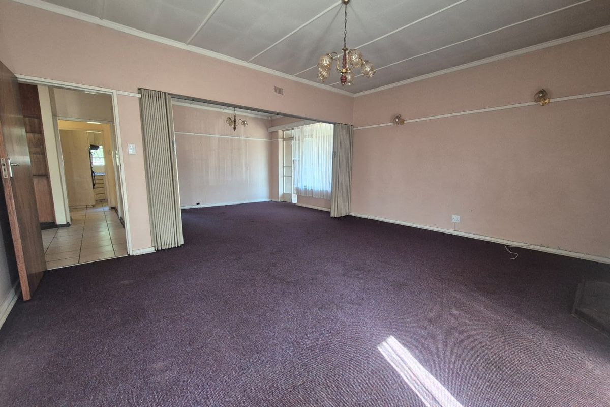 Spacious living area featuring a folding room divider, carpeted flooring, and classic lighting fixtures, offering a blank canvas for renovation and modernization.