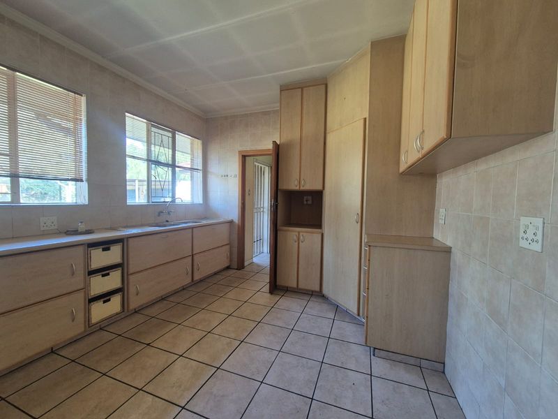 A functional, empty kitchen featuring extensive built-in cabinetry, tiled flooring, and tiled walls, offering a blank canvas for modern renovation.