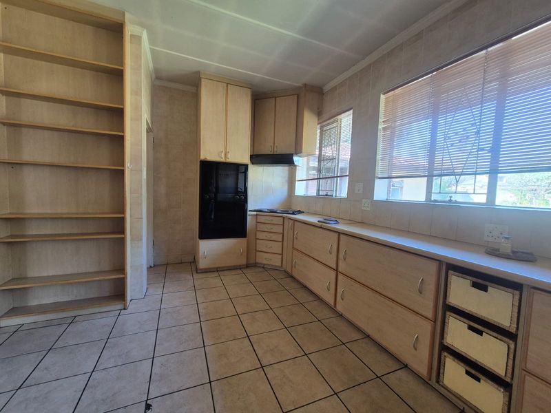 A functional kitchen featuring light wood-tone cabinetry, built-in oven and cooktop, tiled backsplash, and ample storage space with integrated shelving.
