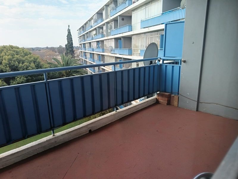 An open-air balcony featuring a metal balustrade and concrete flooring, offering an elevated view of the surrounding apartment complex and greenery.