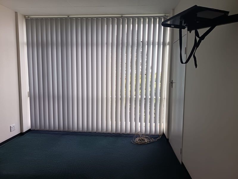 An empty bedroom featuring dark carpeting, vertical window blinds, and a wall-mounted television bracket.