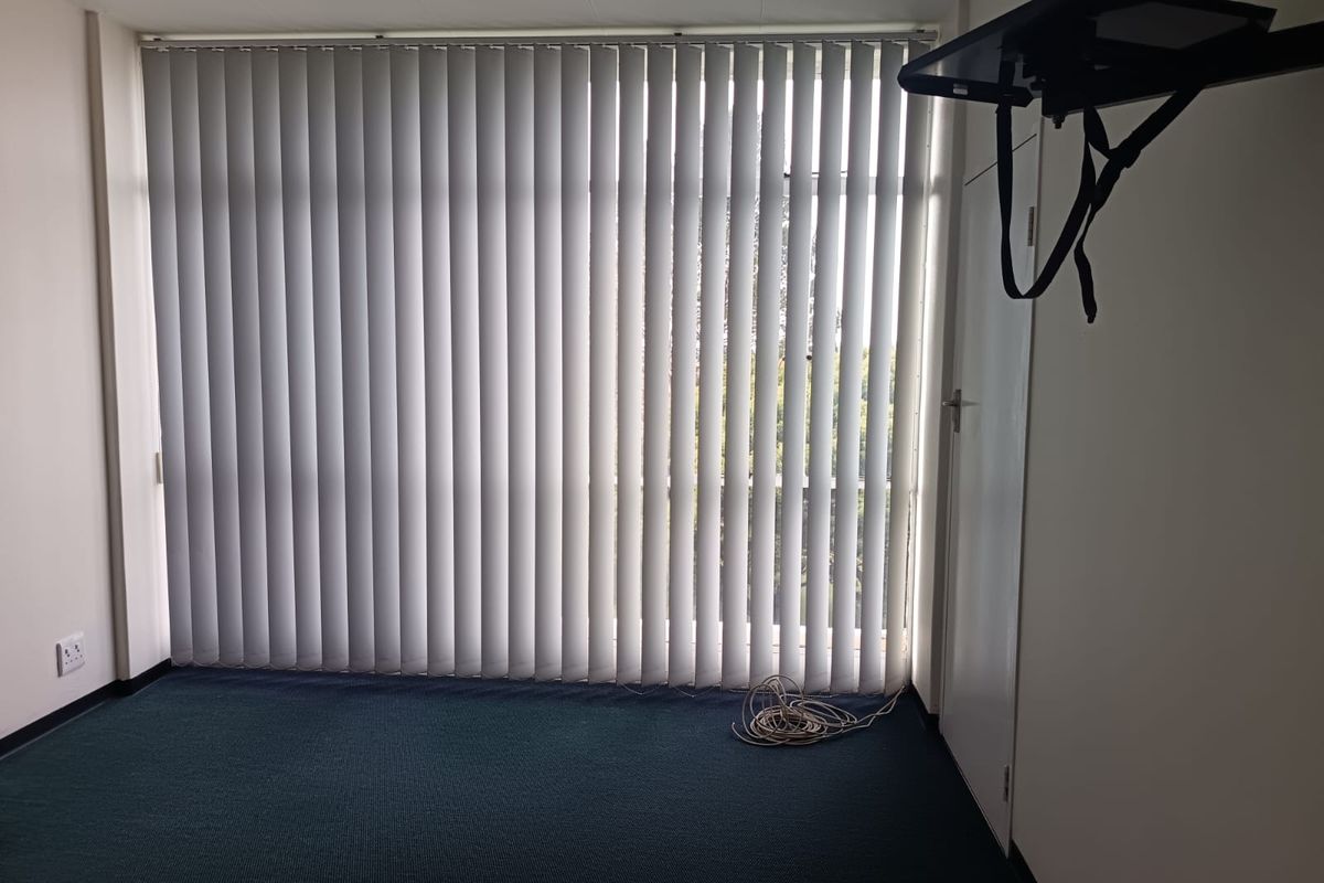 An empty bedroom featuring dark carpeting, vertical window blinds, and a wall-mounted television bracket.